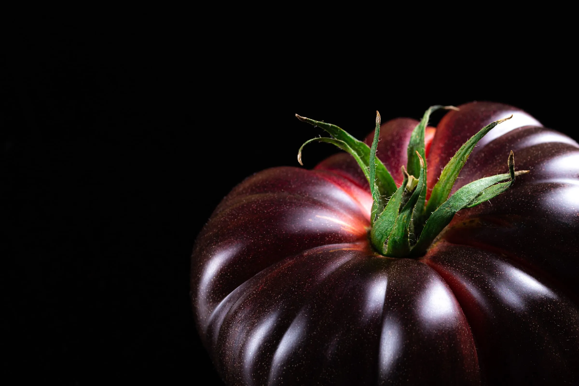 Detalle de la piel oscura y brillante, con el rabillo verde, sobre fondo negro.